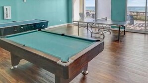 A pool table in a room with teal walls and large windows.