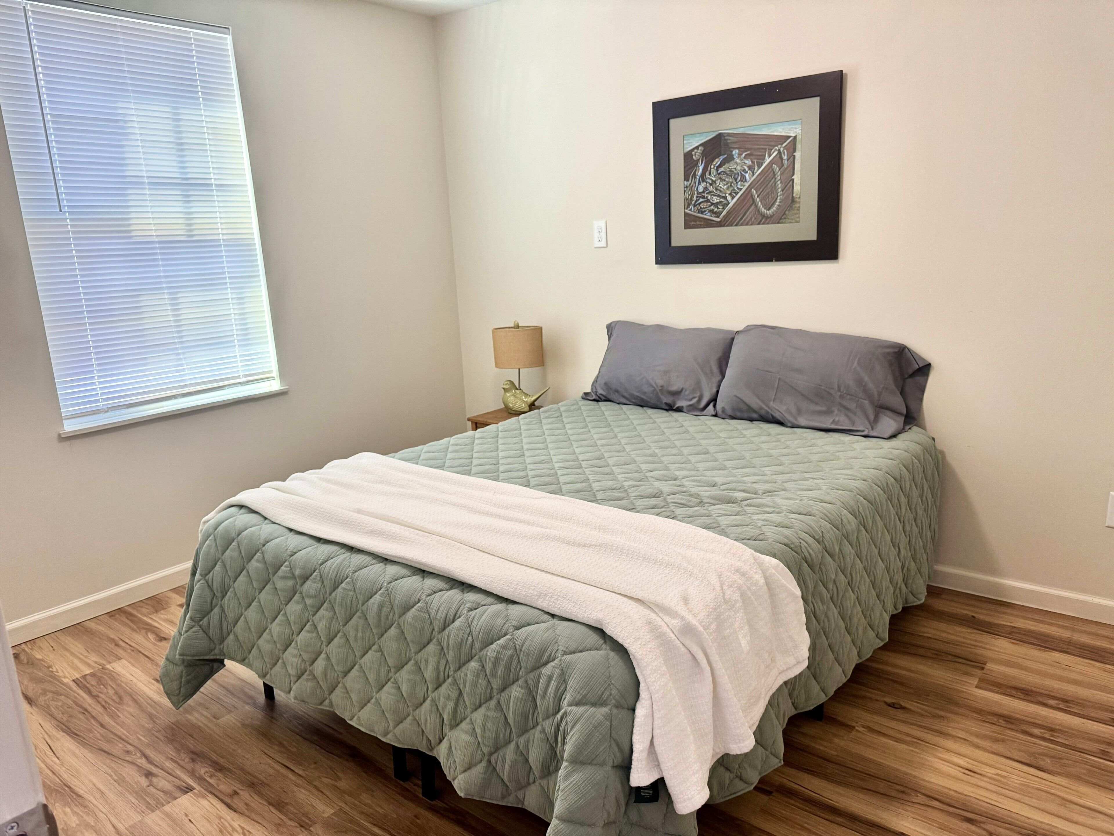 A bedroom with a bed, a nightstand, a lamp, and a framed picture on the wall.