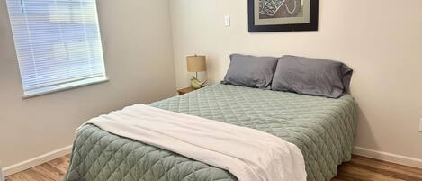 A bedroom with a bed, a nightstand, a lamp, and a framed picture on the wall.