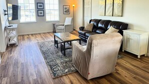 Un salon spacieux doté d’un parquet, d’un canapé en cuir, d’un fauteuil à oreilles, d’une table basse et d’une armoire blanche.