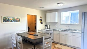Une cuisine moderne avec des meubles blancs, un plan de travail en granit et un coin repas comprenant une table et des chaises en bois.