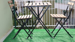 Un balcone con pavimento in erba sintetica verde, due sedie di legno e un tavolo dalla struttura in metallo nero.