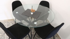 Un tavolo rotondo in vetro con un vaso bianco e un sottopiattino nero. Quattro sedie nere lo circondano.