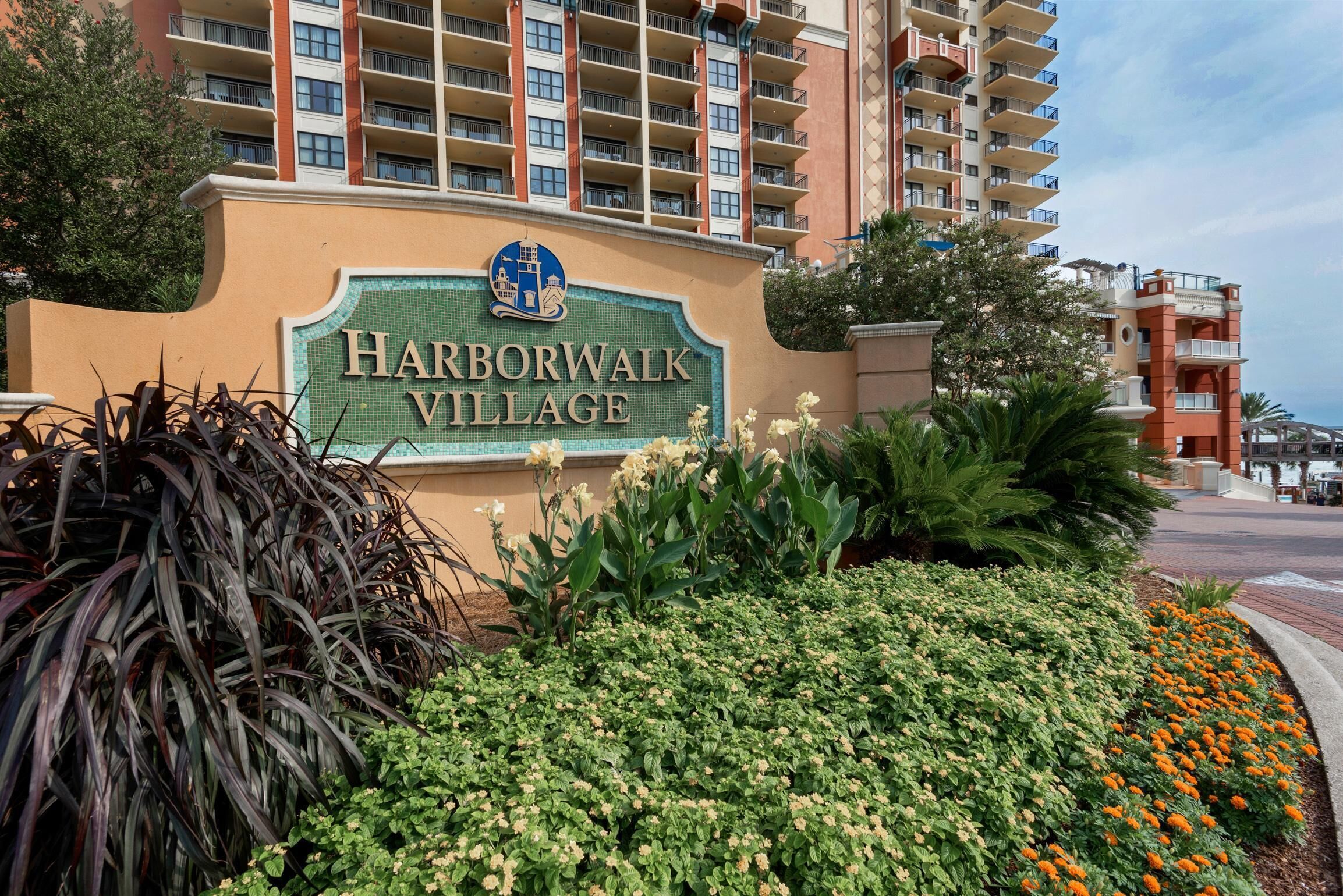 A sign for Harborwalk Village with a view of high-rise buildings in the background.