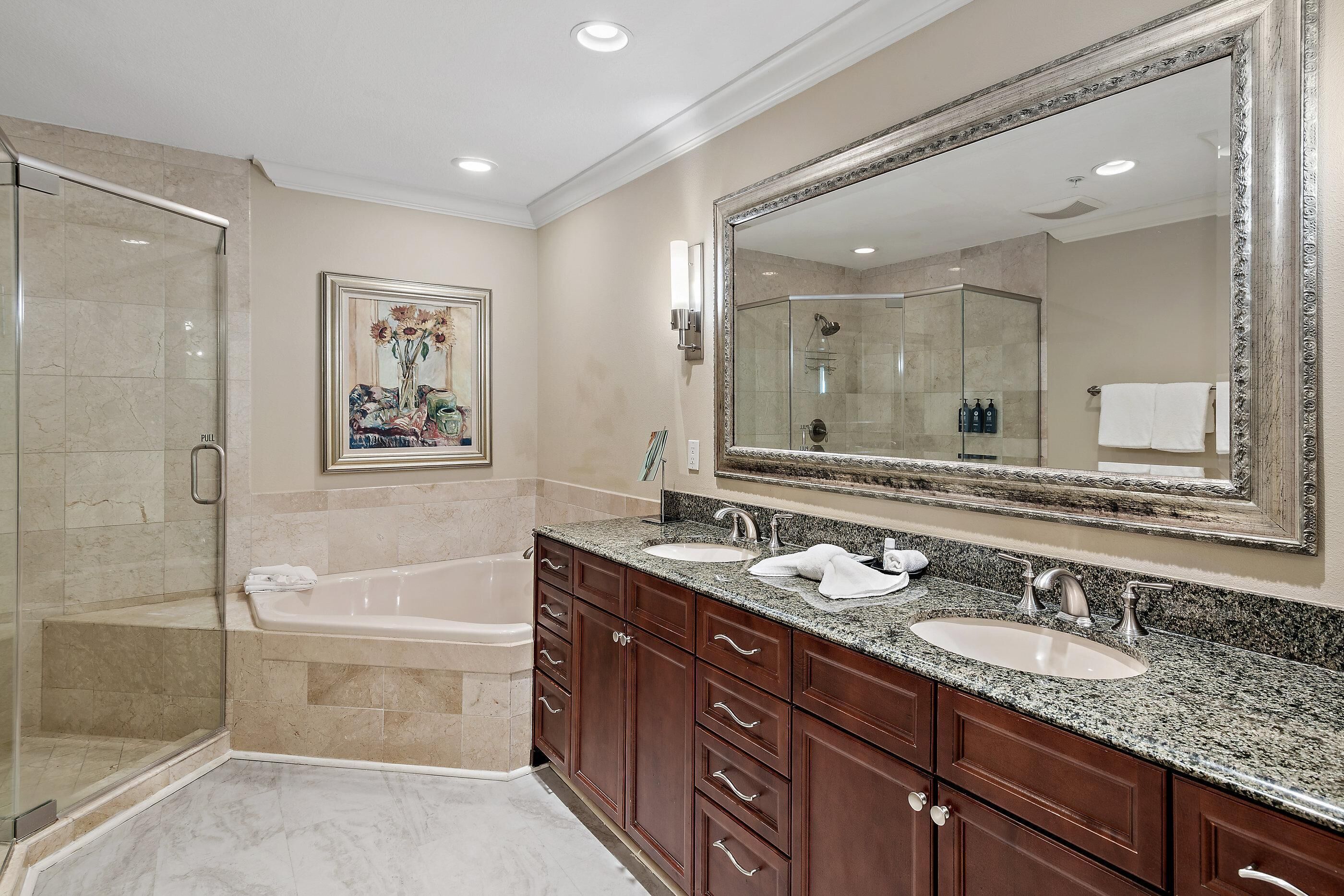 Une salle de bain avec un grand miroir, deux lavabos, une baignoire et une douche.