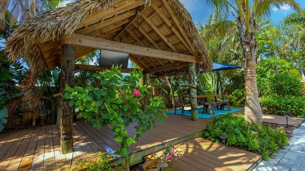 Una terraza de madera con techo de paja, rodeada de exuberante vegetación y palmeras.