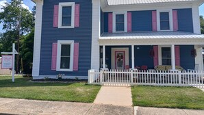 A two-story house with a porch, a small garden, and a sign for 'Pink Ladies on Main Street.' - Pink Lady on Main, Downtown Pilot Mtn, business district. Pet Friendly. (Pilot Mtn)