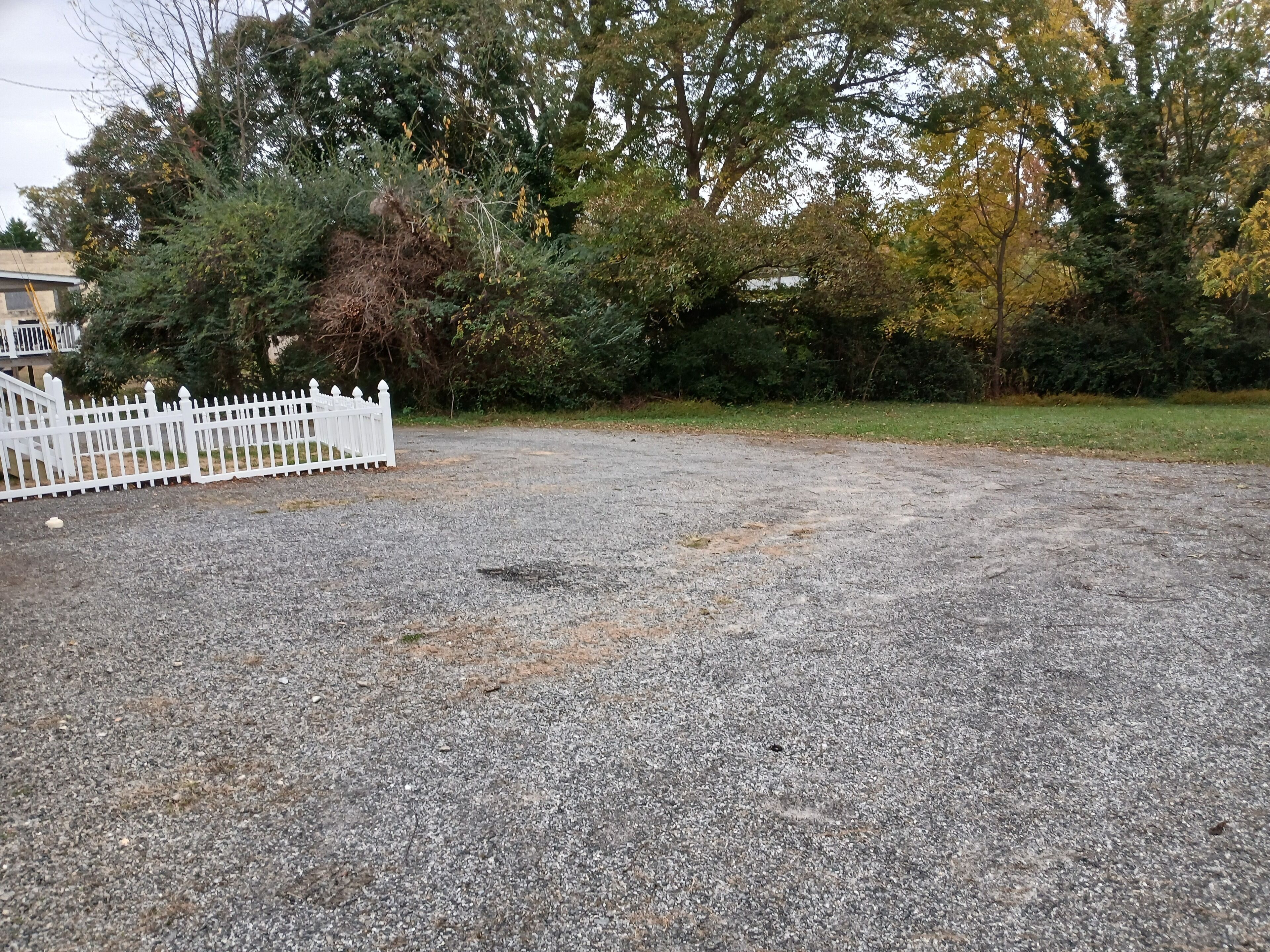 A gravel parking area with a white fence and trees in the background.