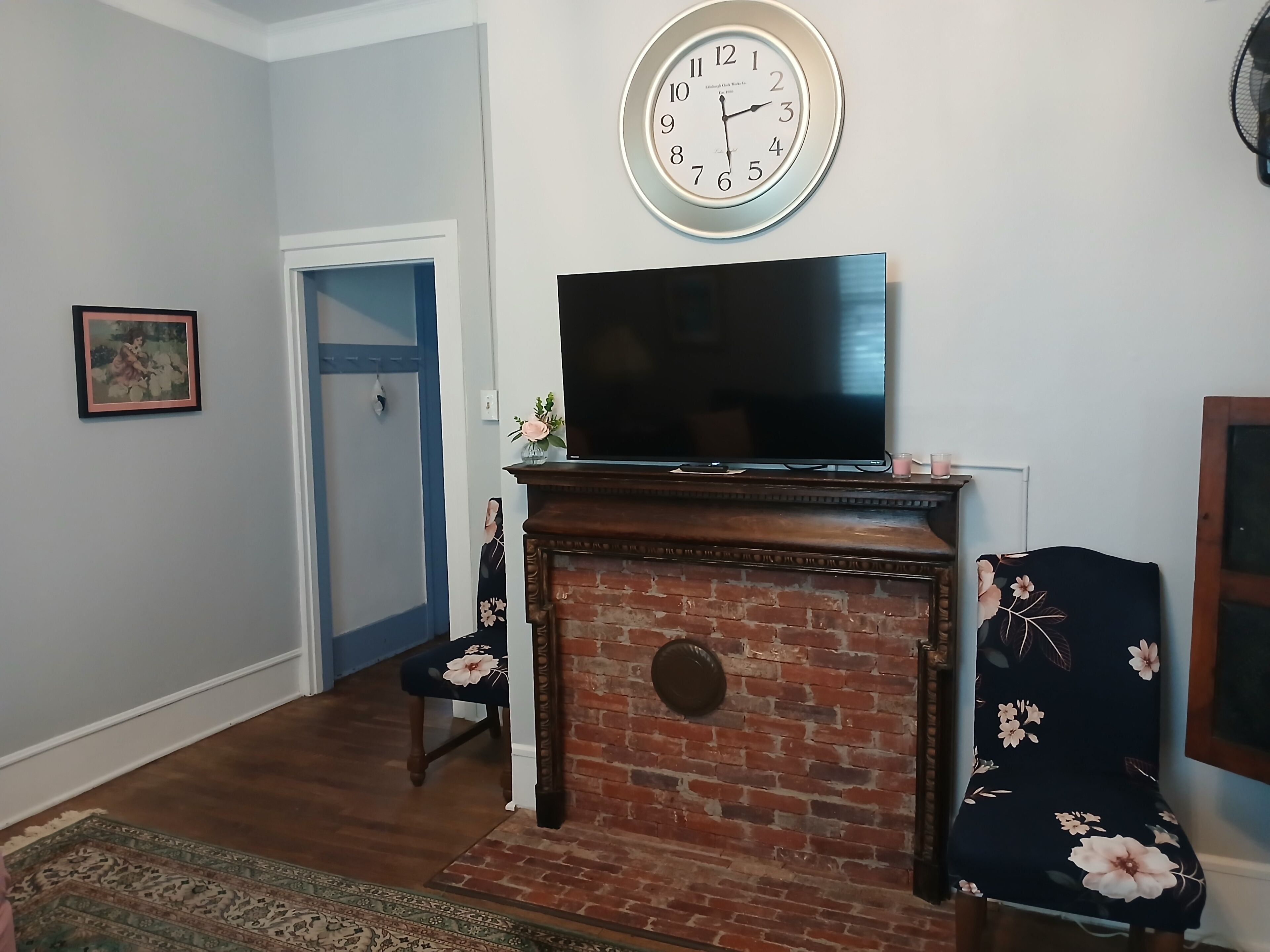 Ein Wohnzimmer mit Kamin aus Ziegelsteinen, einem Flachbildfernseher, einer Uhr und einer Tür.