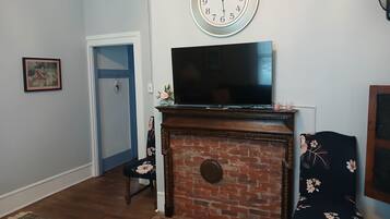 Ein Wohnzimmer mit Kamin aus Ziegelsteinen, einem Flachbildfernseher, einer Uhr und einer Tür.