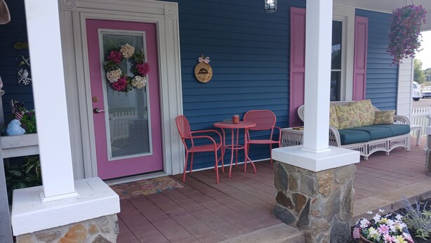 A porch with a stone column, a wicker sofa, a table with chairs, and a hanging flower basket. - Pink Lady on Main, Downtown Pilot Mtn, business district. Pet Friendly. (Pilot Mtn)