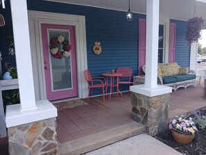 A porch with a stone column, a wicker sofa, a table with chairs, and a hanging flower basket.