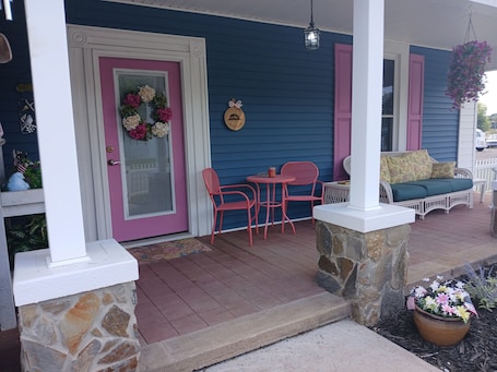 A porch with a stone column, a wicker sofa, a table with chairs, and a hanging flower basket.