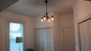A room with a chandelier, a window with blinds, a teal armchair, and a set of white doors.