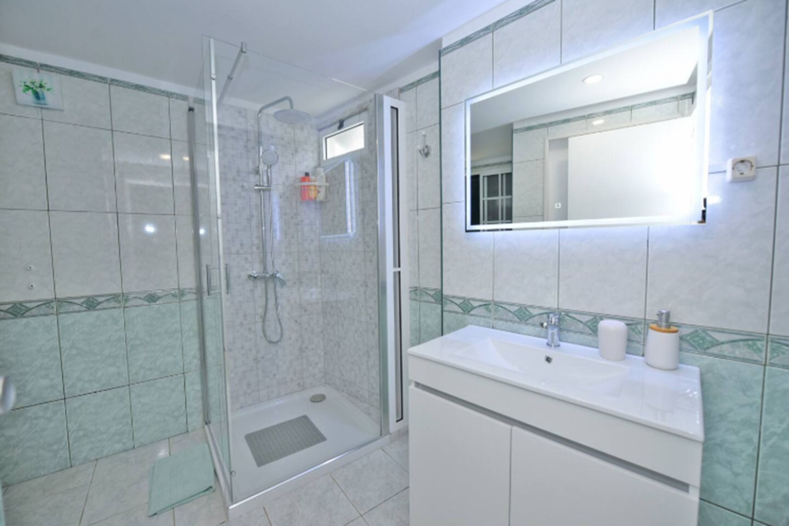 A bathroom with a glass-enclosed shower, a white sink with two bottles, and a mirror above the sink.