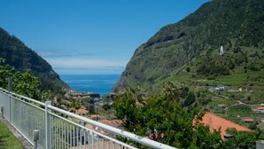 A coastal landscape with a view of the sea, green hills, and a white building with a red roof. - Cantinho das Feiteiras by Homie (São Vicente)
