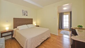 A bedroom with a large bed, bedside tables, a nightstand, a window with curtains, and a door leading to another room. - Cantinho das Feiteiras by Homie (São Vicente)