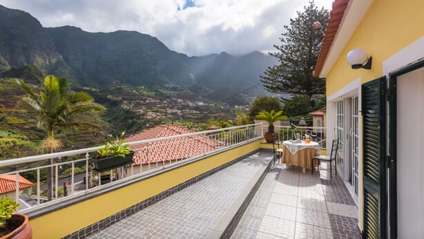 A balcony with a tiled floor, potted plants, and a table with chairs. - Cantinho das Feiteiras by Homie (São Vicente)