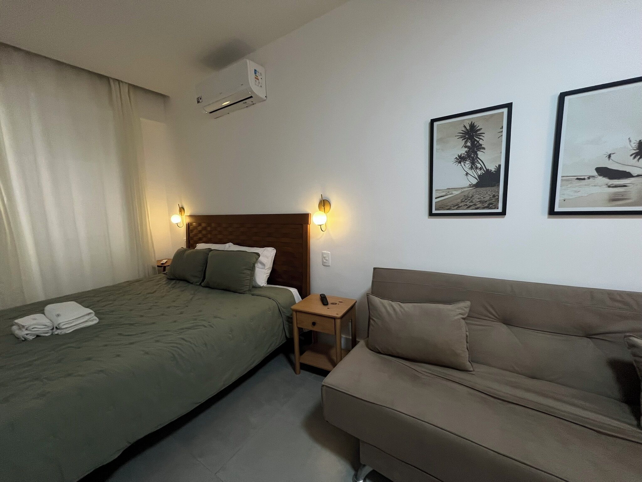 Una habitación de hotel con una cama, un sofá y dos lámparas de pared.