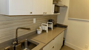 Una cocina con gabinetes blancos, un lavamanos de acero inoxidable, un microondas y una encimera con un portavasos para cuchillos.