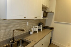 A kitchen with white cabinets, a stainless steel sink, a microwave, and a countertop with a knife holder. - Studio apartment across from Copacabana Beach. (Rio de Janeiro)