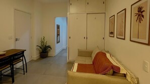 Un pasillo con una mesa de comedor y sillas, una planta en maceta, un sofá con una manta y un armario con varias puertas.