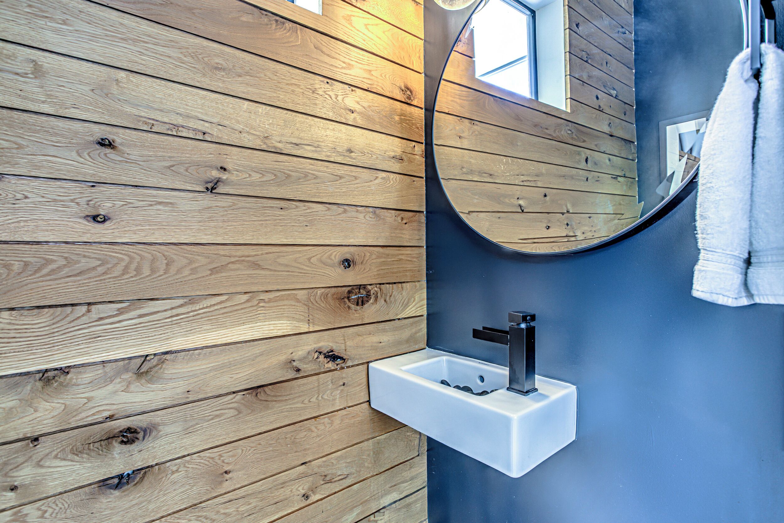 Ein Badezimmer mit Holzwandverkleidung, einem weißen Waschbecken und einem Spiegel.