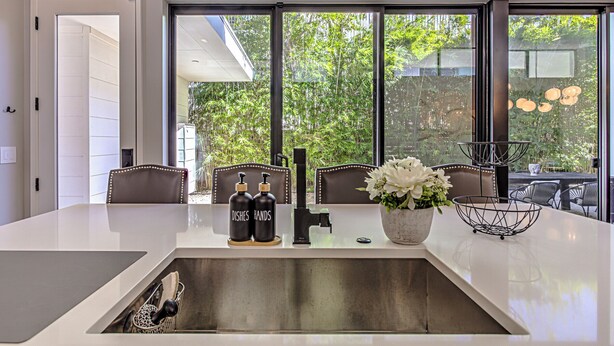 Una cocina moderna con una isla grande, dos sillas, un fregadero y una ventana con vistas a zonas verdes.