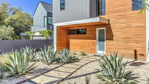 Una casa moderna de dos plantas con fachada de madera y un sendero de piedra que lleva a la entrada.