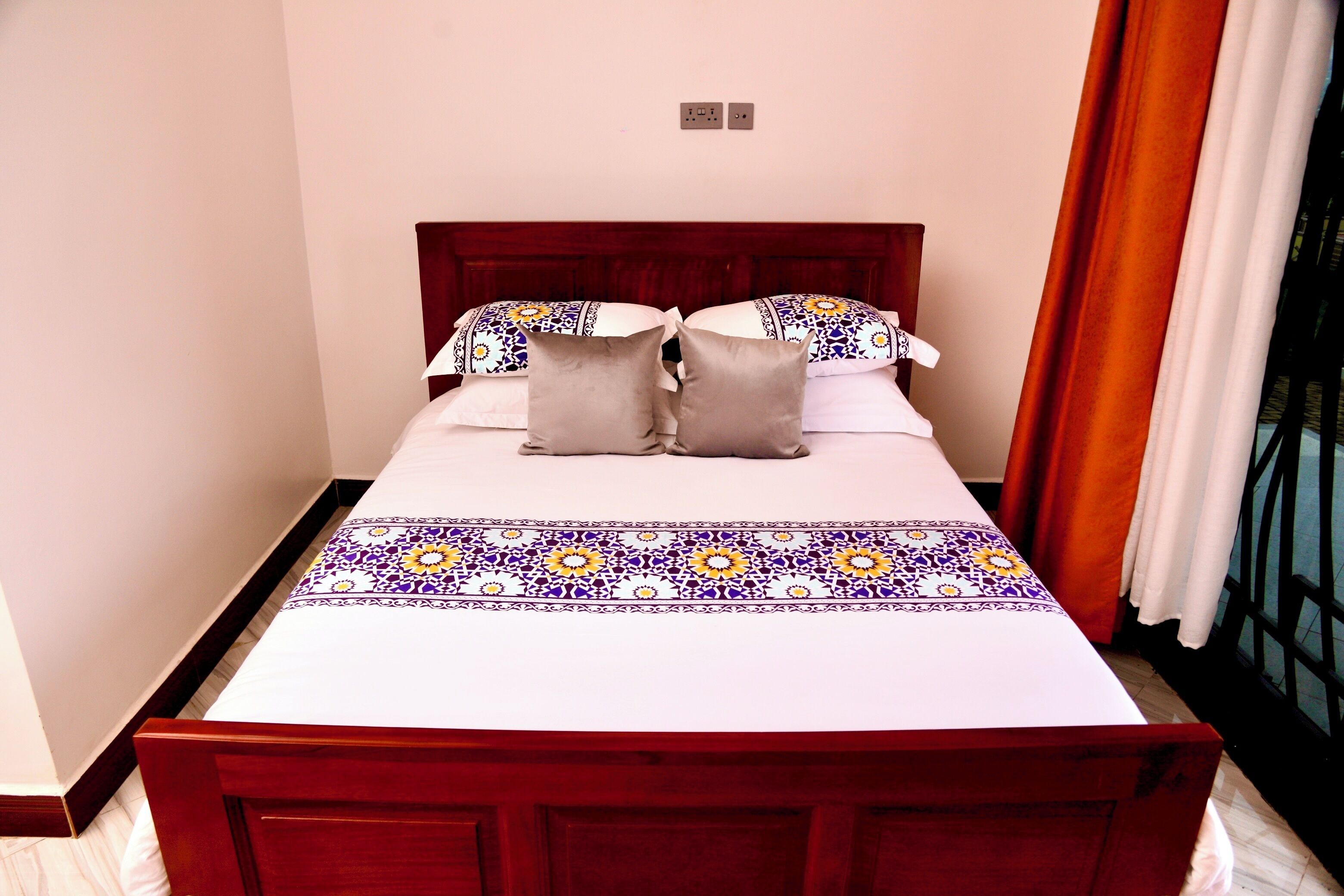 A neatly made bed with a patterned bedspread, a wooden headboard, and a window with curtains.