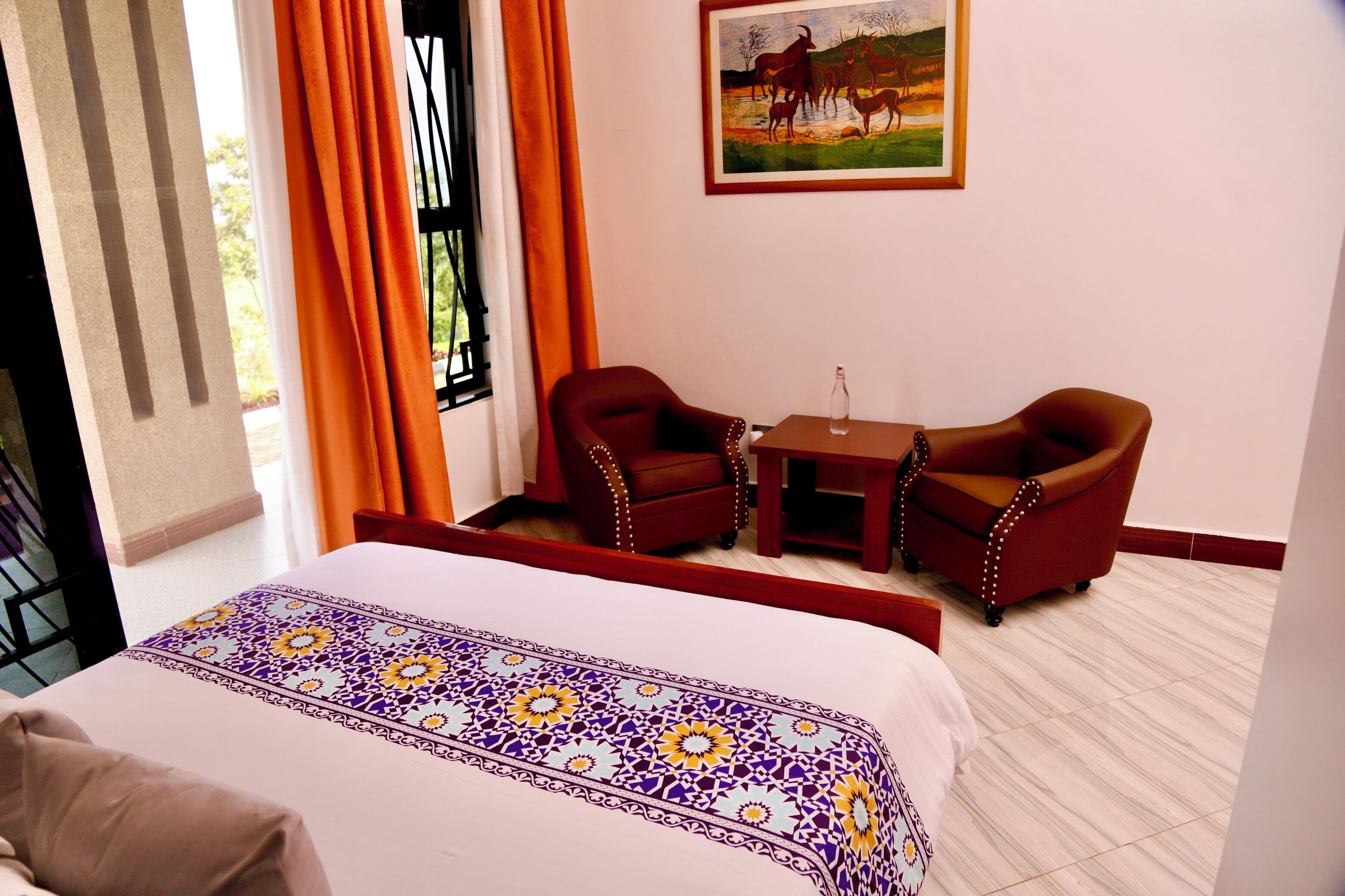 Una habitación de hotel con una cama, dos sillones, una mesita y un cuadro en la pared.