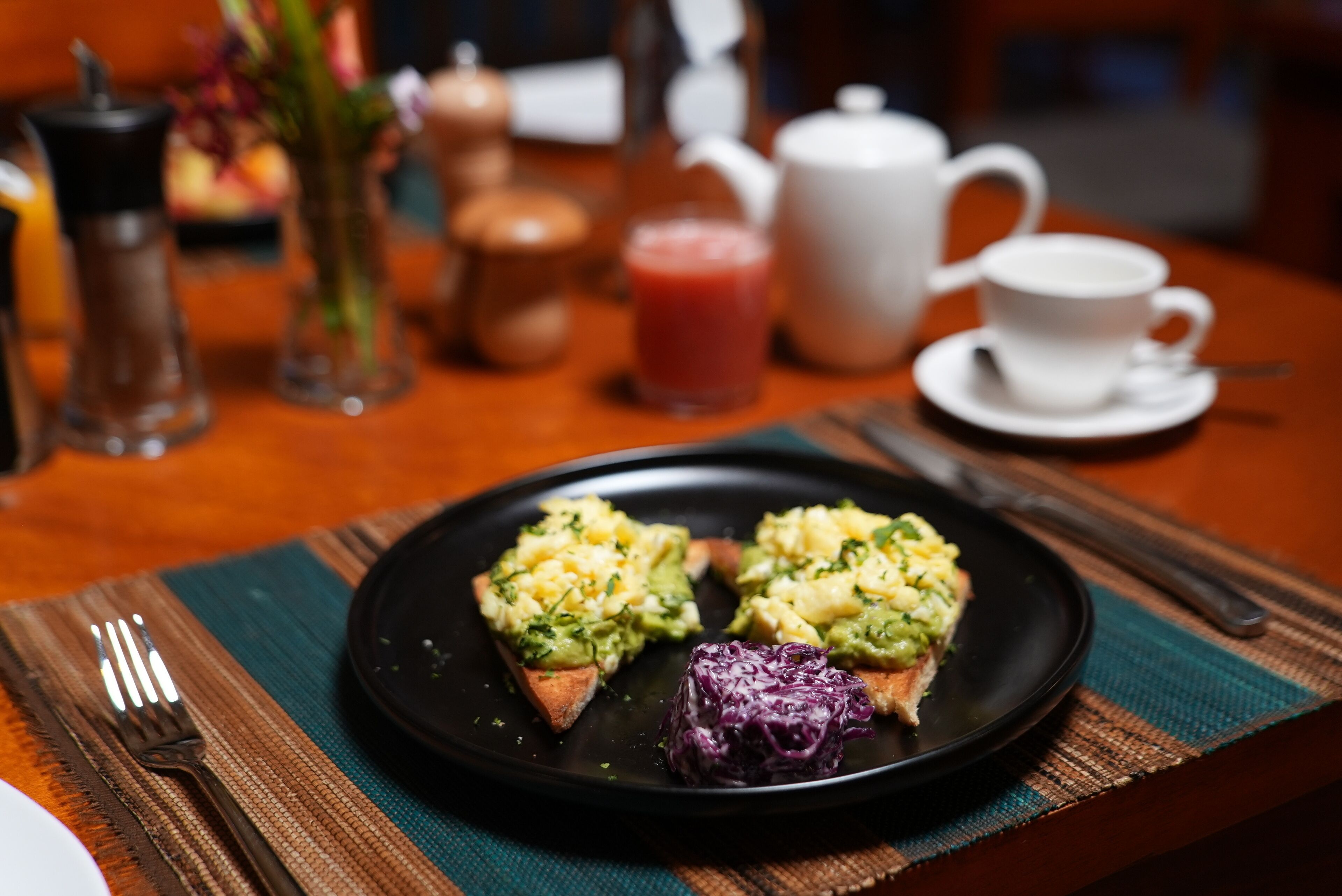 A breakfast setting with toast topped with avocado and a side of red cabbage.
