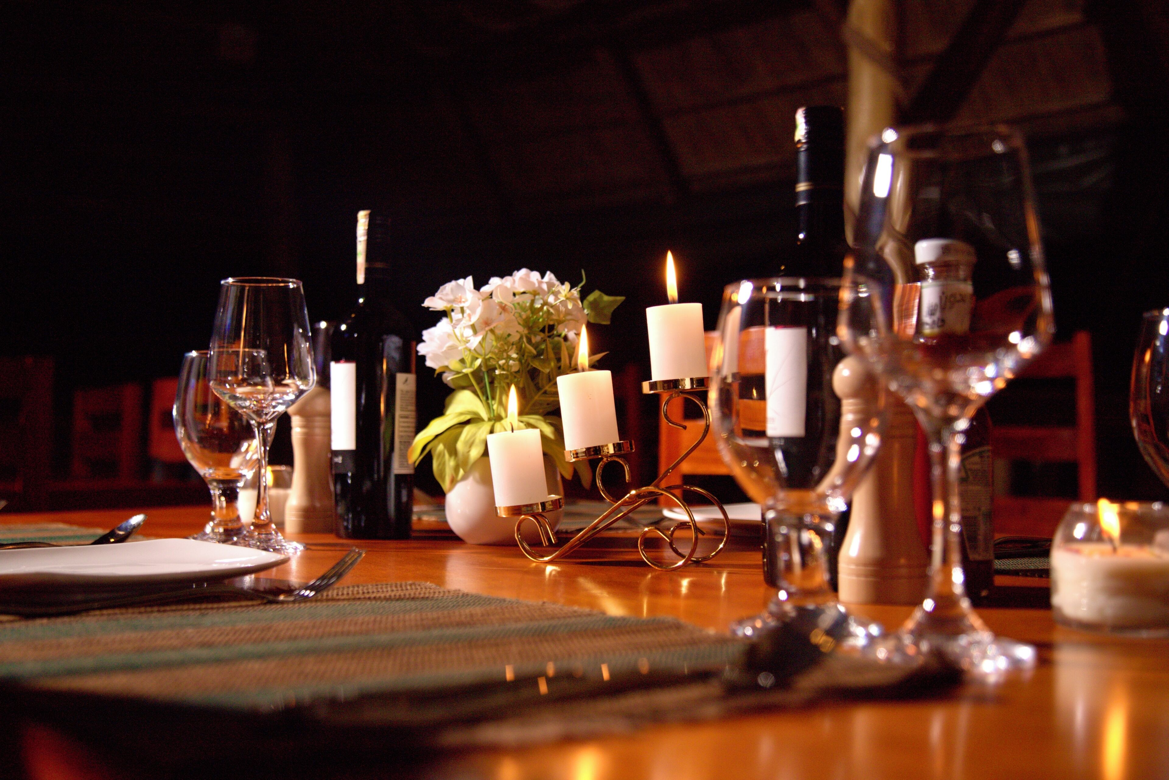 Una mesa de comedor dispuesta con velas, copas de vino y un florero.