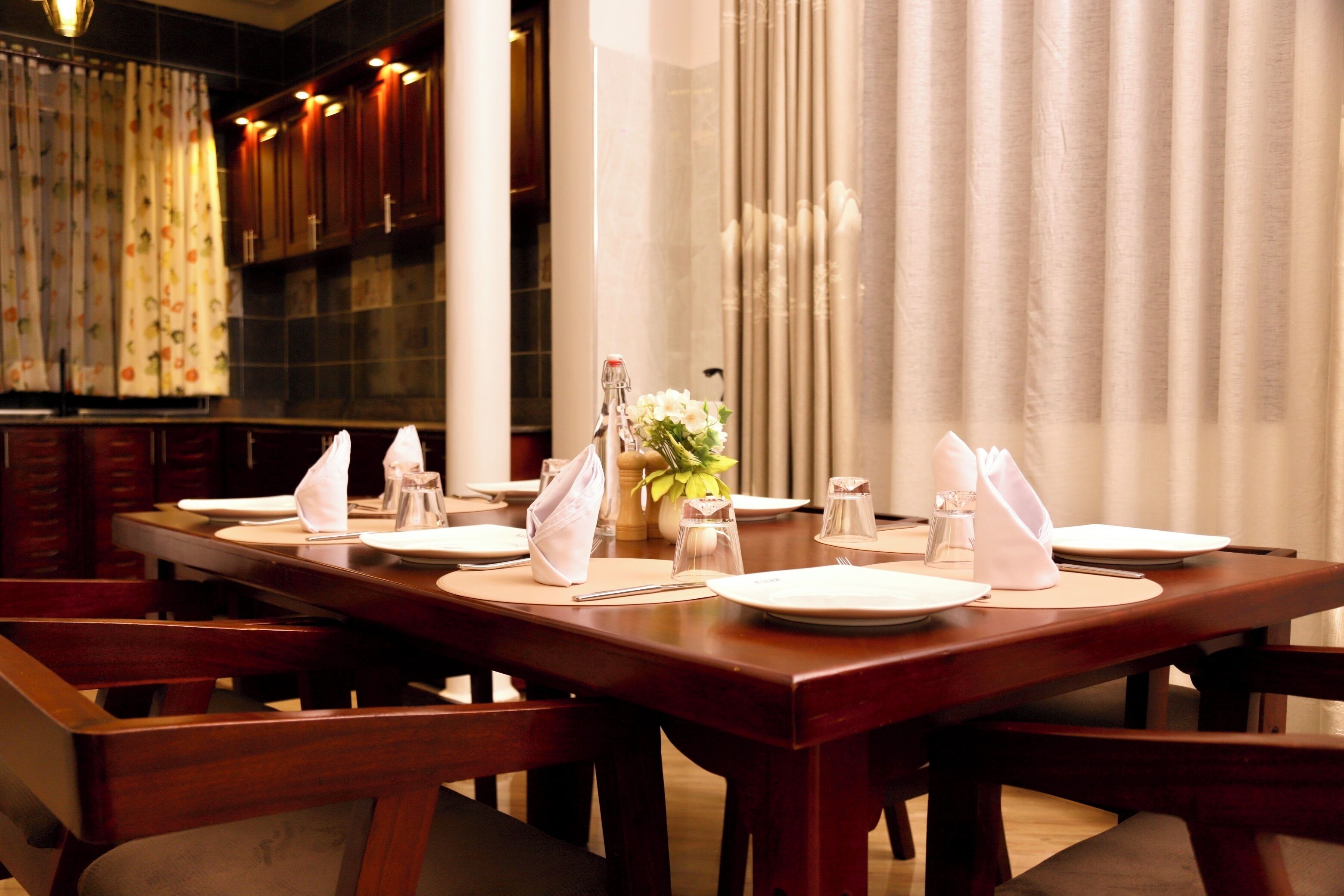 A dining table set for six with white plates, napkins, and cutlery. There are salt and pepper shakers, a vase with flowers, and a candle on the table.