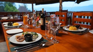 A dining table set with plates of food, wine glasses, and a bottle of wine. - Bird Hill Resort Ug (Kabale)