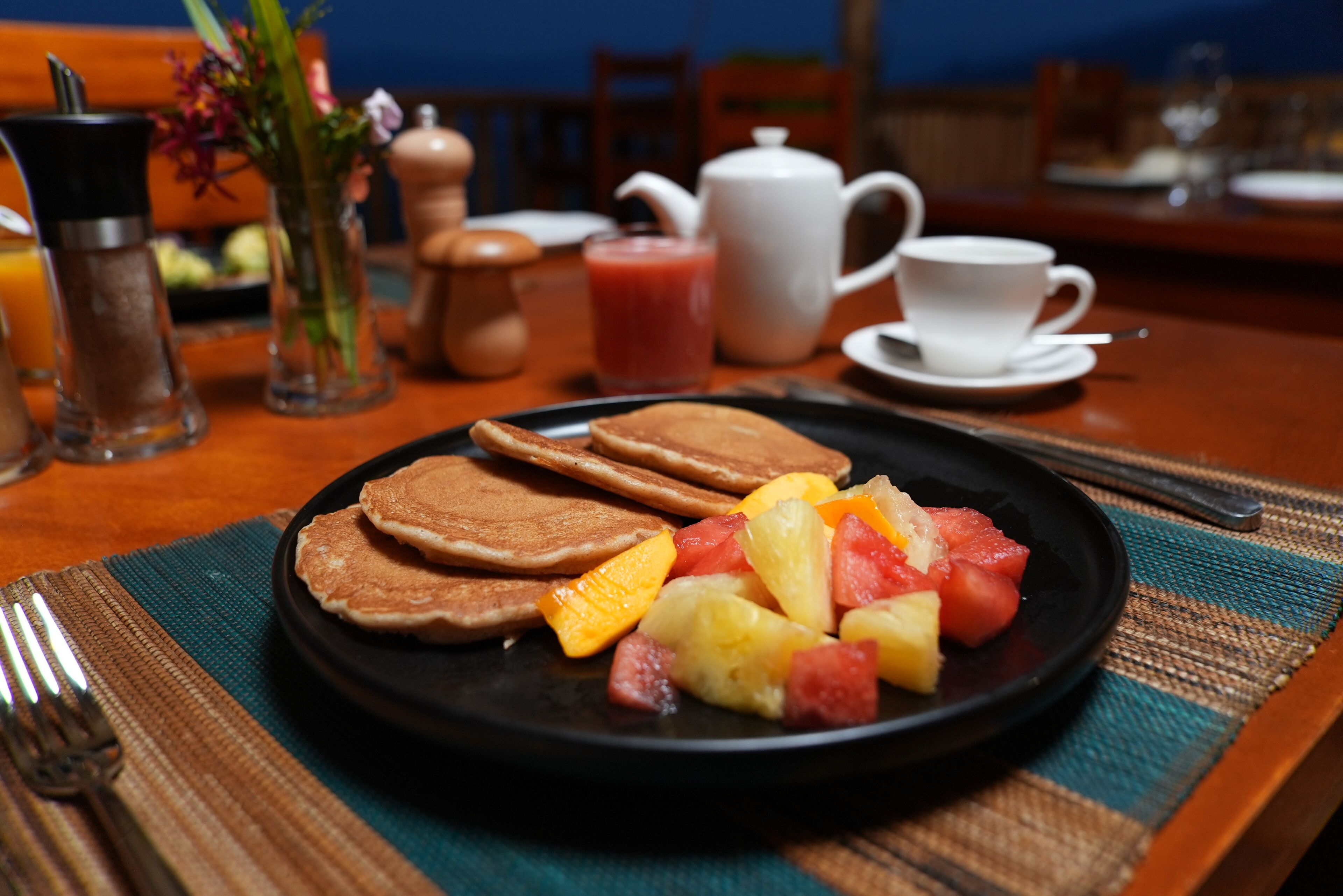 A breakfast setting with pancakes, fruit, and a cup of coffee on a table.
