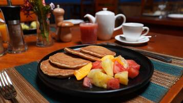 Una escena de desayuno con panqueques, fruta y una taza de café sobre una mesa.