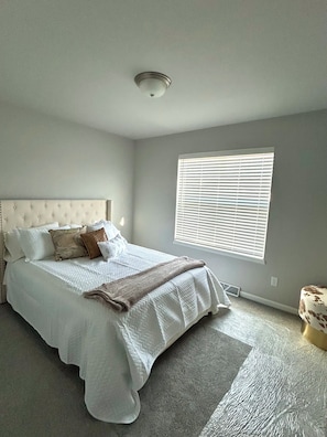 A bedroom with a large bed, a headboard, a window with blinds, and a ceiling light. - New and Modern 3-bedroom charming house 20 minutes from downtown Madison. (Madison)