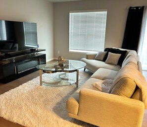 A living room with a sofa, a glass coffee table, a TV, and a black entertainment unit. - New and Modern 3-bedroom charming house 20 minutes from downtown Madison. (Madison)
