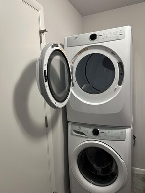 A front-loading washer and dryer stacked in a laundry room with a door on the left. - New and Modern 3-bedroom charming house 20 minutes from downtown Madison. (Madison)