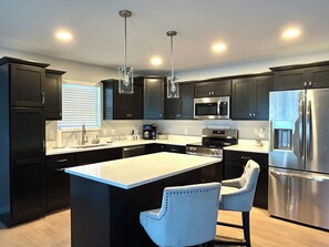 A modern kitchen with dark cabinets, stainless steel appliances, and a central island with bar stools. - New and Modern 3-bedroom charming house 20 minutes from downtown Madison. (Madison)