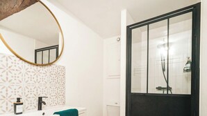 Une salle de bain moderne avec un meuble-lavabo blanc, un miroir rond, des toilettes et un espace douche.