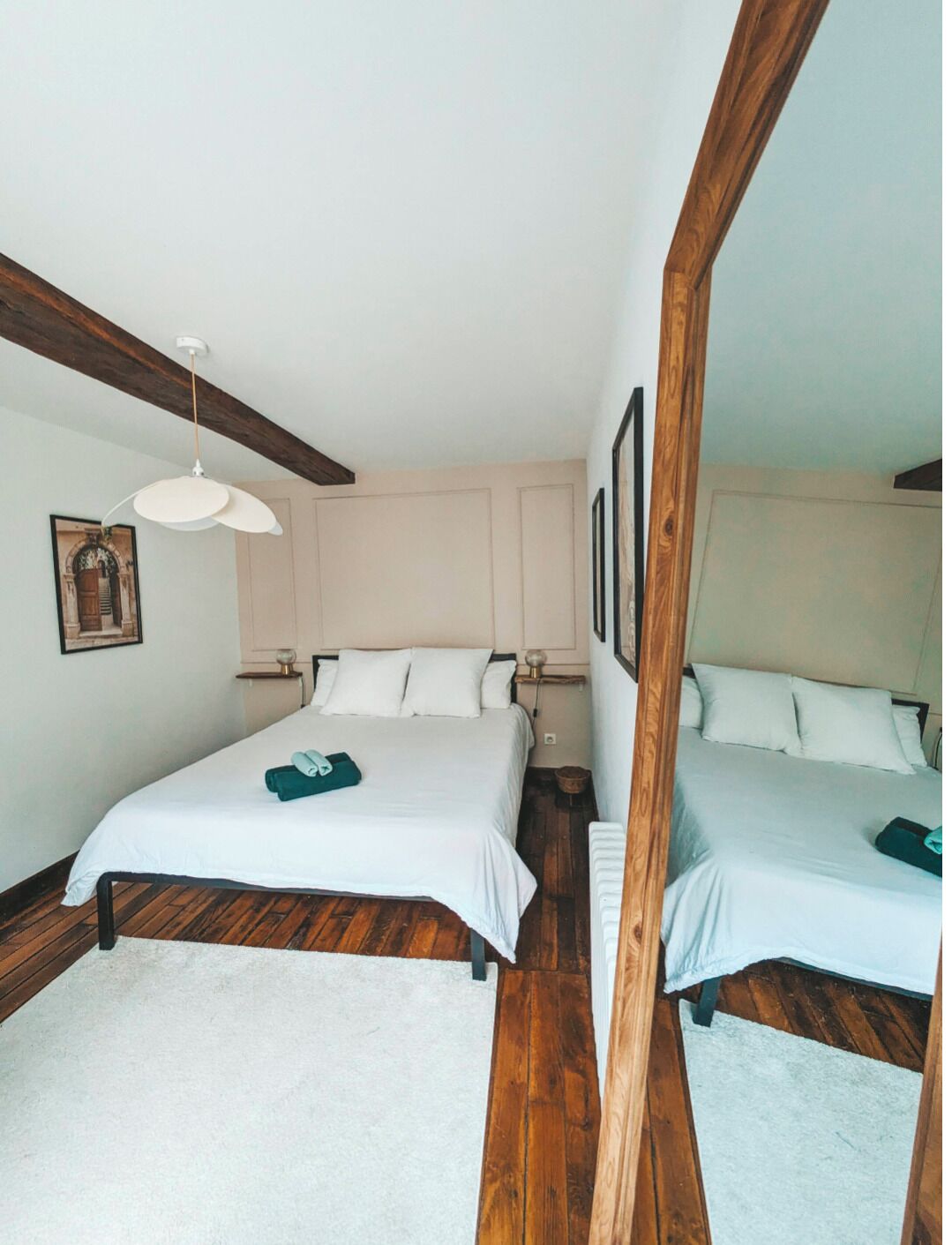 Un dormitorio con dos camas, suelo de madera, techo blanco y un espejo grande.