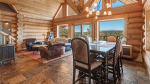 A log cabin interior with a dining area, fireplace, and large windows offering a view of the landscape. - 45-Acre Florissant Ranch Cabin & Stable (Florissant)