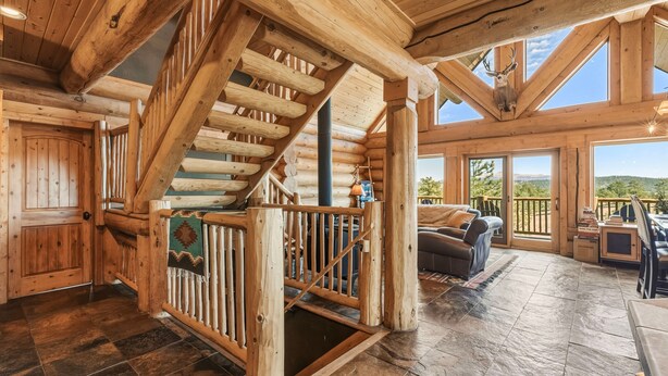 A log cabin interior with a wooden staircase, stone flooring, and a view of the outdoors. - 45-Acre Florissant Ranch Cabin & Stable (Florissant)