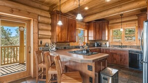A wooden cabin kitchen with a central island, wooden chairs, and a built-in sink. - 45-Acre Florissant Ranch Cabin & Stable (Florissant)