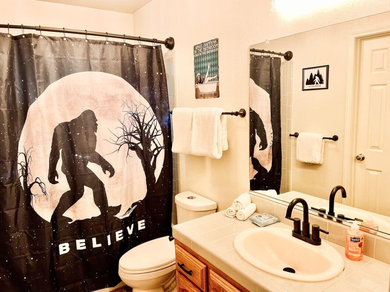 A bathroom with a shower curtain featuring a silhouette of a person and trees, a toilet, a sink with a mirror, and a towel rack.
