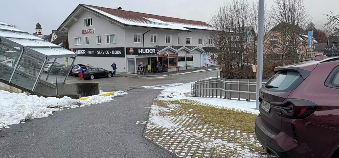 A building with a sign reading "HUBER RENT - SERVICE - MODE" and a car parked in front.