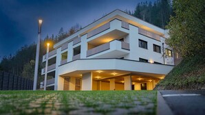 A modern multi-story building with balconies, a covered parking area, and a well-lit entrance.