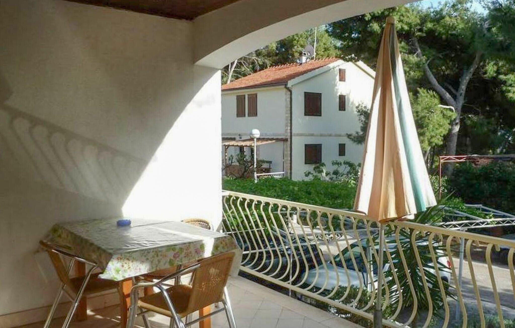 A balcony with a table and chairs, a metal railing, and a view of a building with a red roof.